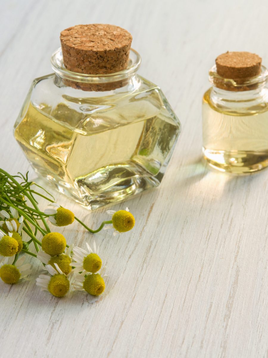 Chamomile flower water or oil in glass bottle on wooden table background. Aromatherapy, cosmetics or SPA concept