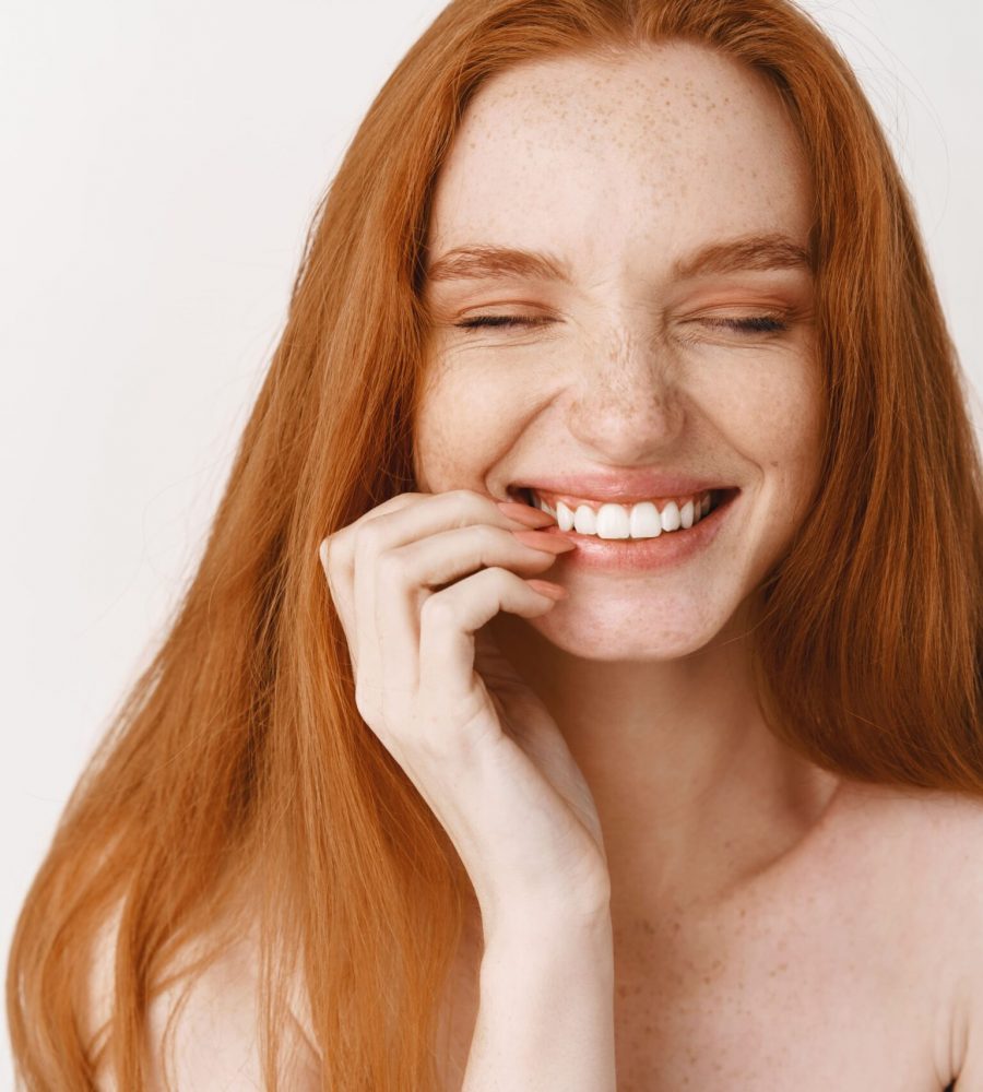 close-up-of-happy-redhead-woman-with-pale-no-makeup-skin-and-perfect-smile-laughing-and-looking-joyful-standing-naked-over-white-wall (1)